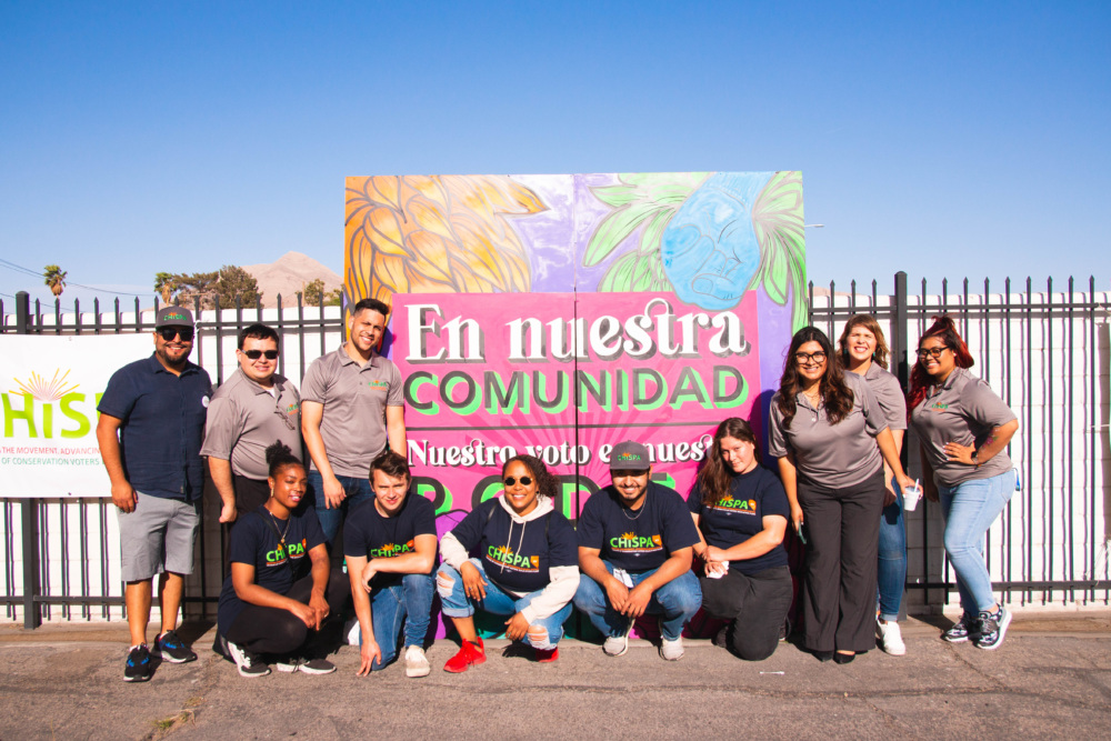 Chispa staff pose in front of sign about voting.