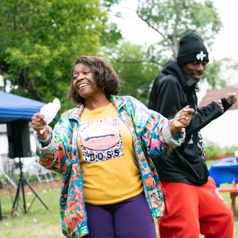 Adults dance happily at a Democracy For All community event in a park