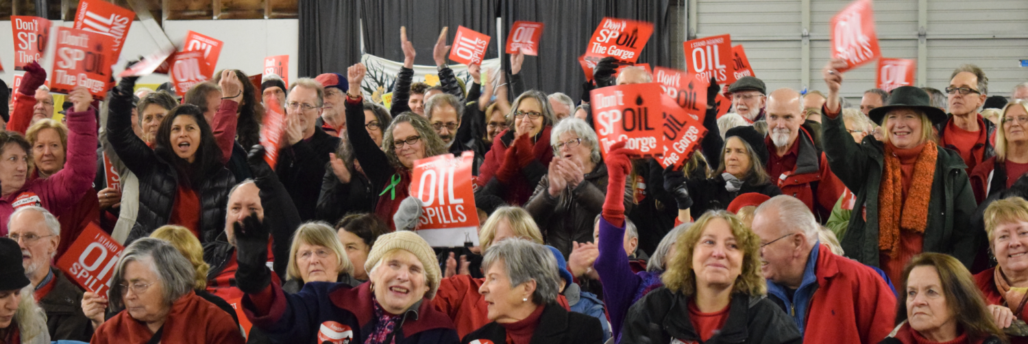 A crowd waves signs that say "I Stand Against Oil Spills"