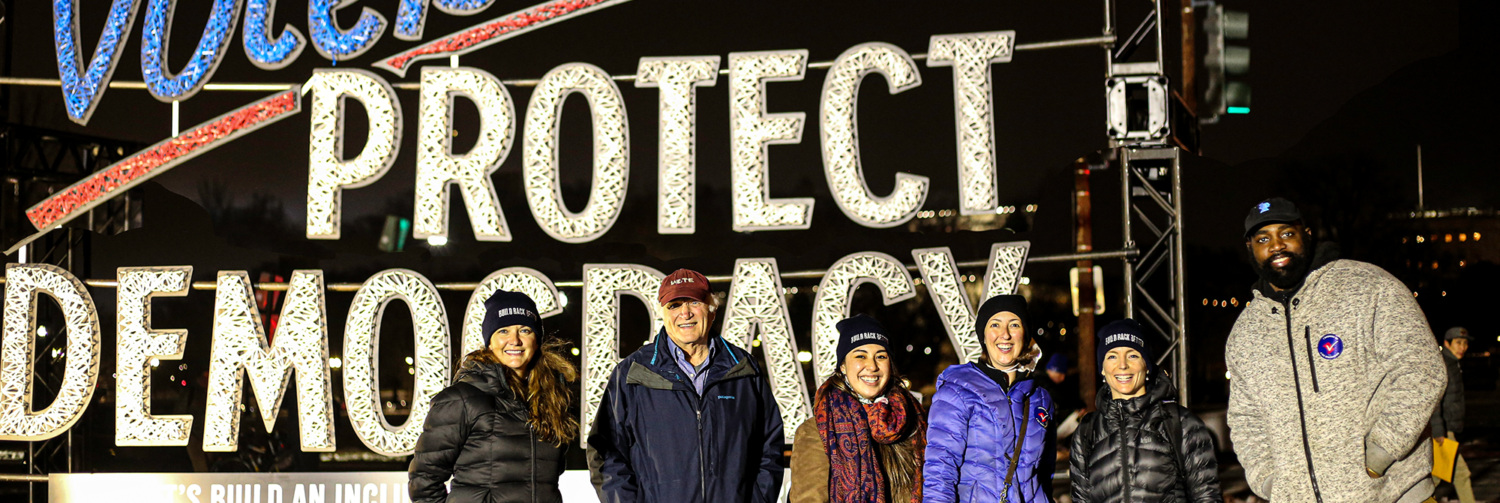 LCVEF staff standing in front of an art installation sign that reads "Protect Democracy".