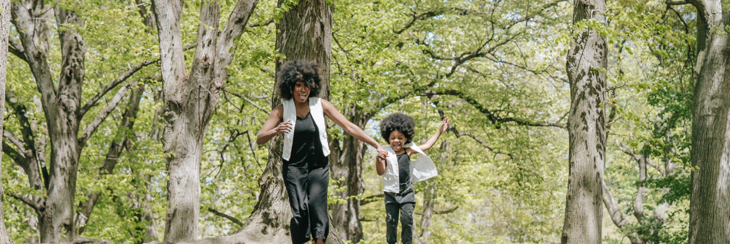 A mother and child hold hands while jumping in nature