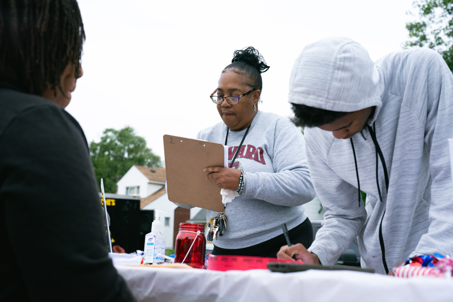 Two community members stand over a table and fill out forms on clipboards