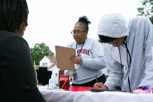 Two community members stand over a table and fill out forms on clipboards