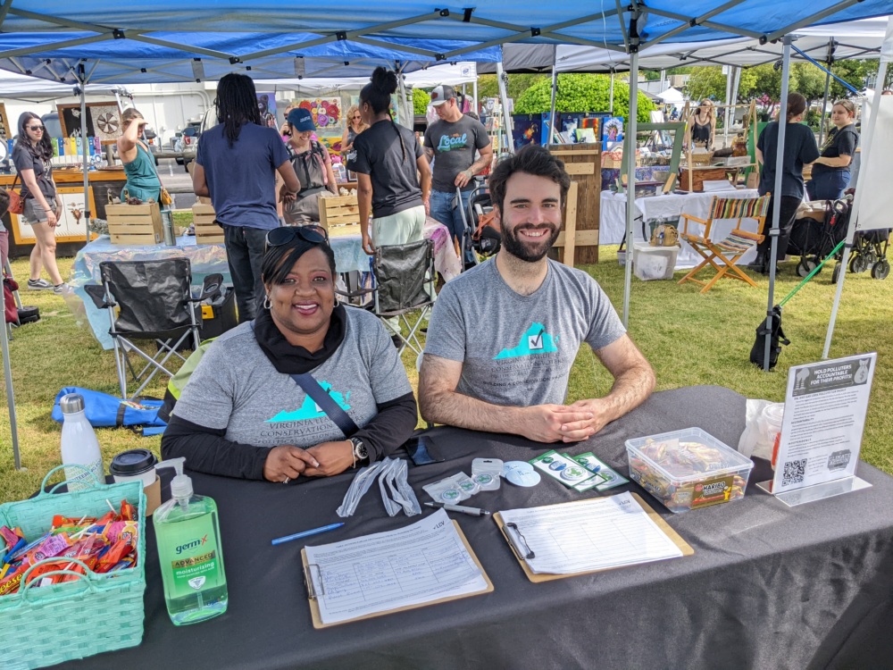 Personnel from the Virginia League sit at a table with marketing collateral and sign up sheets at an outdoor event