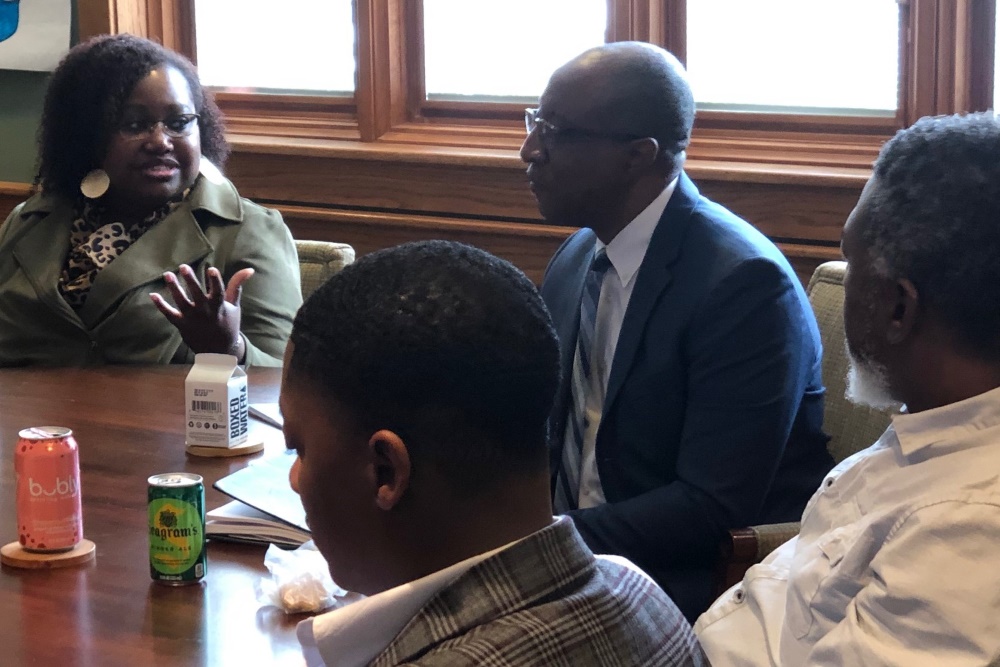 A woman seated at a conference table speaks while three men seated near her listen.