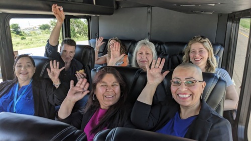 Colorado Boards & Commissions Fellows on a bus headed to an event smile and wave at the camera.