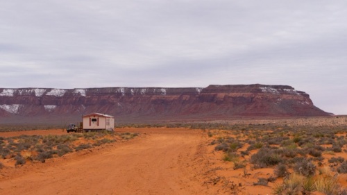 Wide shot of a lone house by a desert road with a butte in the distance.