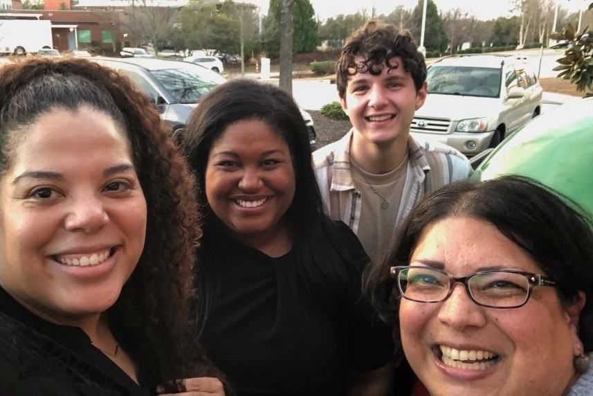Four people pose outside for a group selfie.