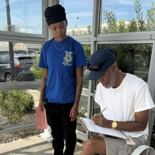 A volunteer watches as a member of the public fills out their voter registration