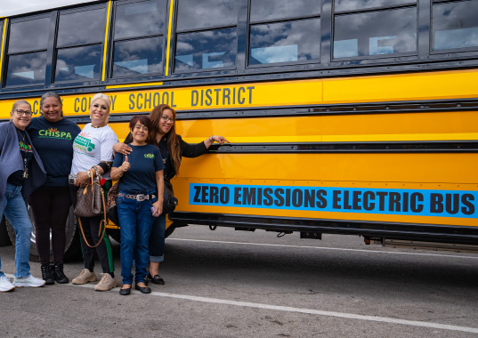 Chispa activists pose next to a zero emissions electric school bus