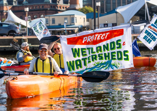 Activists kayak with signs calling to protect wetlands and watersheds