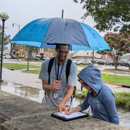 A volunteer holds an umbrella in the rain as a member of the public registers to vote